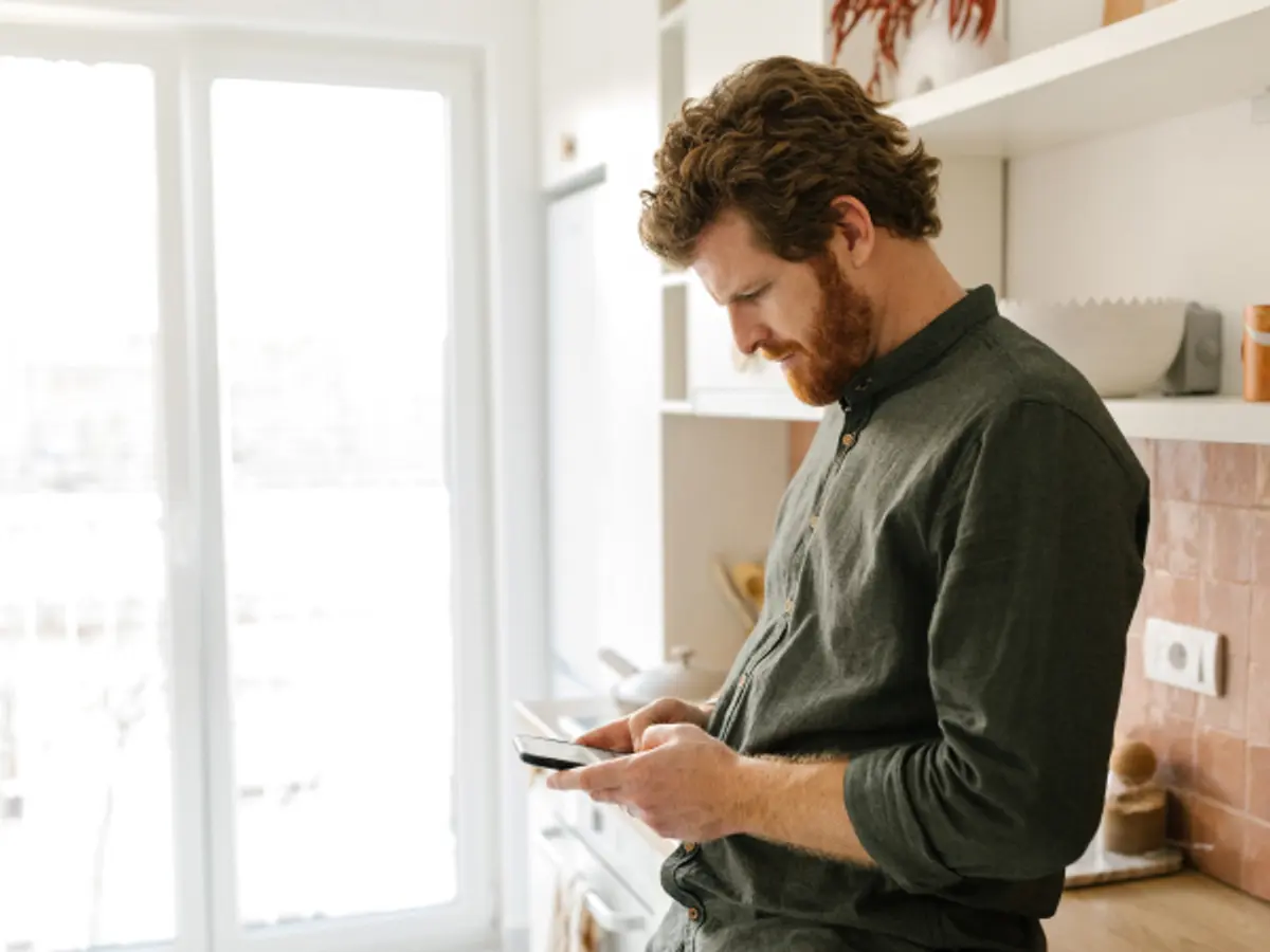 Man wearing green shirt heads down on his phone concentrating. 